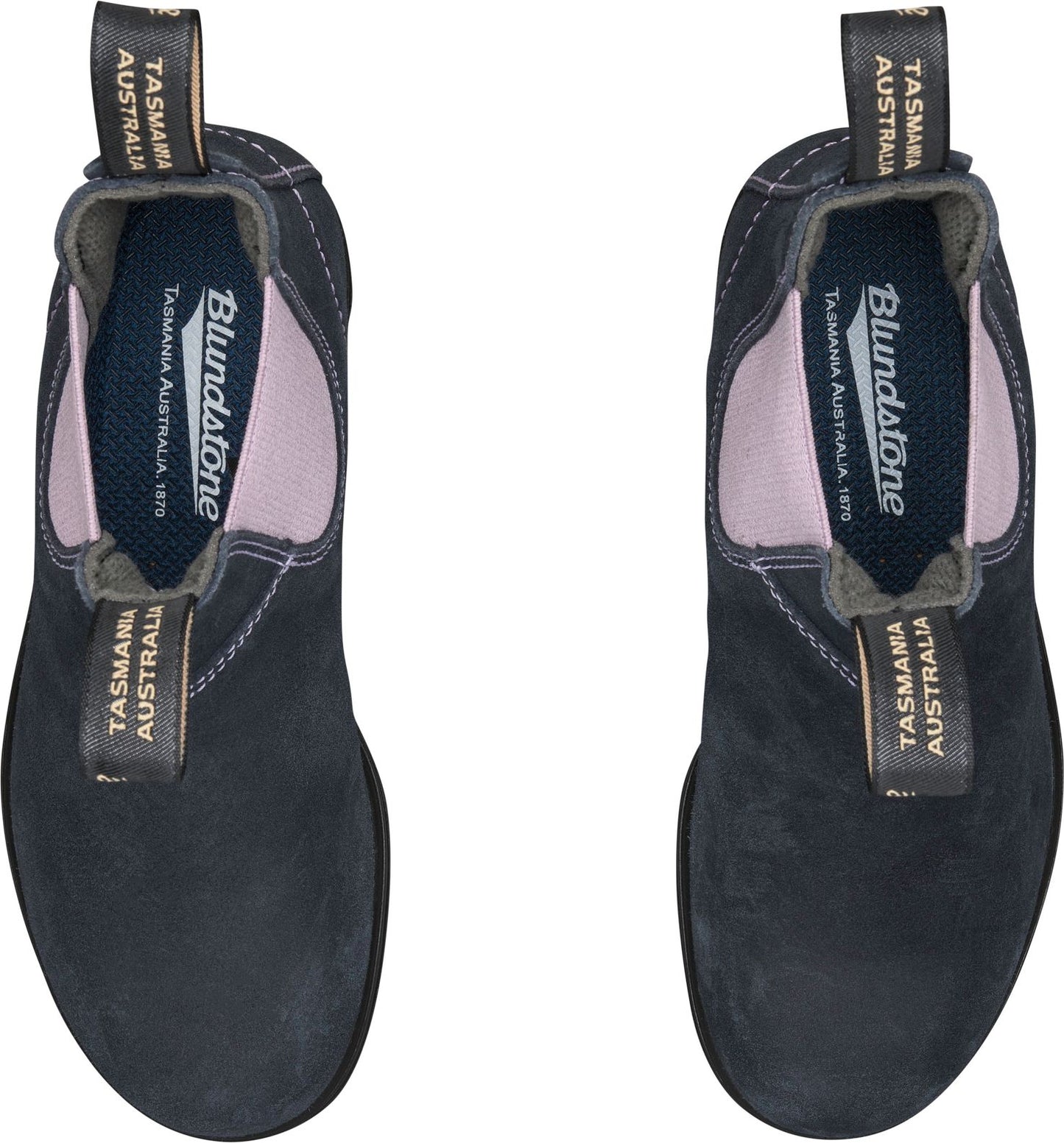 Two Blundstone boots are presented from a top-down perspective, showing their black suede exteriors, pink elastic side panels, and gray fabric pull tabs. The insides of the boots reveal a gray lining and insole with the text "Blundstone TASMANIA AUSTRALIA 1870" and "TASMANIA AUSTRALIA" displayed prominently.