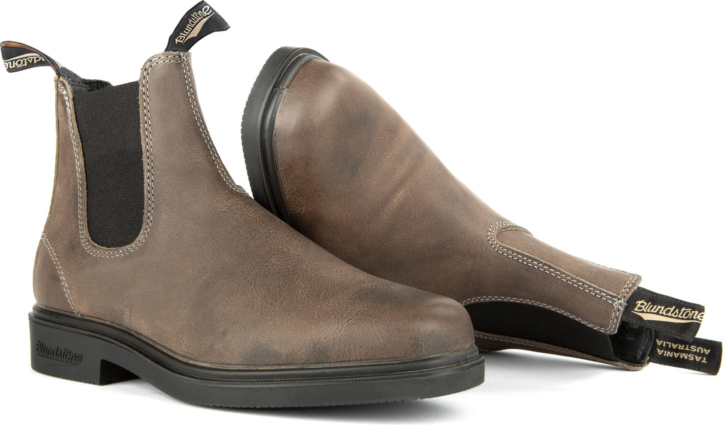 Pair of leather Chelsea boots in taupe with black soles and elastic side panels, one standing and one lying on its side.