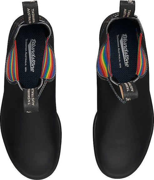 Overhead view of two black ankle boots with rainbow-colored elastic side panels, printed text inside reading 'Blundstone, Tasmania Australia 1870'.