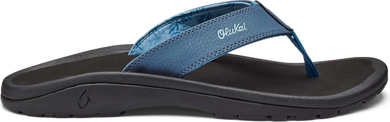 A side view of a dark sole sandal with a blue strap that has the word "Olukai" on it.