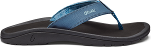 A side view of a dark sole sandal with a blue strap that has the word "Olukai" on it.