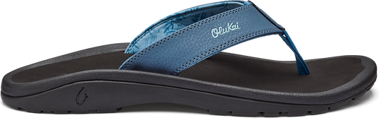 A side view of a dark sole sandal with a blue strap that has the word "Olukai" on it.