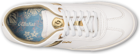 A white OluKai-branded women's sneaker with white laces, a gold logo and gold trim.