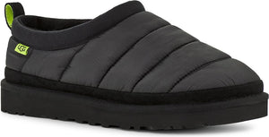 A charcoal-gray slipper with horizontal stitched lines is displayed, featuring a black platform sole, collar, heel pull, and a small lime green label.